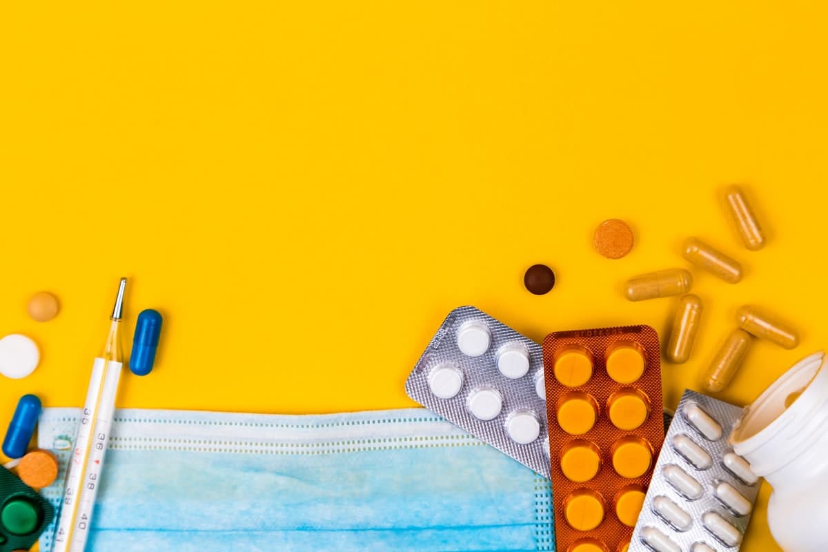 An assortment of pills, capsules and a thermometer on a yellow background