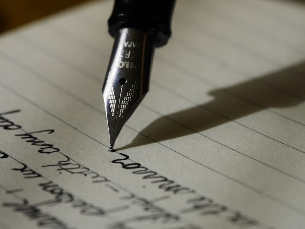 A fountain pen writing cursive on lined paper